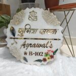 Handcrafted resin nameplate for home entrance – personalized with family name and floral design Custom epoxy resin nameplate with gold flakes and wooden base for house decor Elegant resin name board with marble texture and engraved couple names Personalized resin nameplate for main door with 3D flowers and metallic finish Unique handmade resin nameplate with modern calligraphy and glossy finish